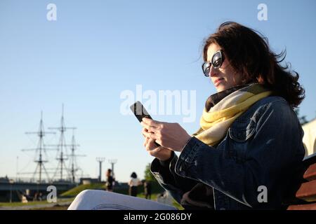 La ragazza con gli occhiali guarda lo schermo dello smartphone. Foto Stock