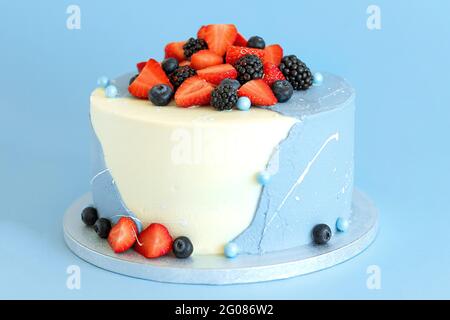 Torta di compleanno blu e bianca con fragole e mirtilli su sfondo blu. Dolci fatti in casa Foto Stock