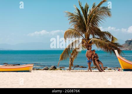 Felice coppia rilassante sulla spiaggia di sabbia vicino palme Foto Stock