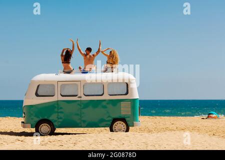 Vista posteriore degli amici seduti in cima all'autobus retrò sulla spiaggia Foto Stock