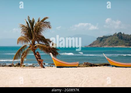 Bella donna in costume da bagno rilassante vicino palme sulla spiaggia Foto Stock