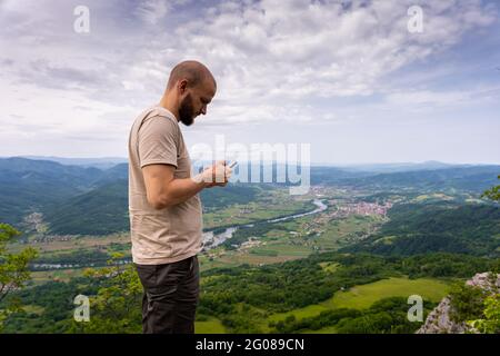 Giovane adulto che controlla il suo telefono con uno splendido scenario sullo sfondo Foto Stock