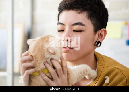 Primo piano di giovane donna tombboy asiatica in abbigliamento casual tenuta e guardando il suo gatto affettuosamente Foto Stock