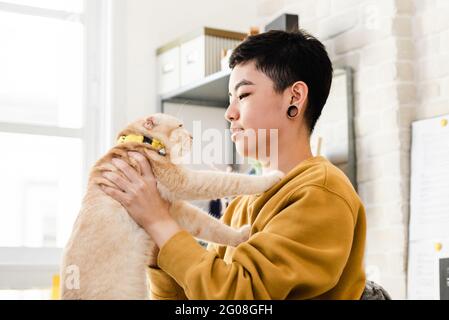 Giovane donna da ragazzo asiatica in abbigliamento casual che tiene e guarda il suo gatto affettuosamente Foto Stock