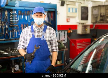 Uomo di lavoro in maschera protettiva in piedi vicino all'auto al servizio di riparazione auto Foto Stock