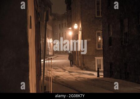 Un uomo cammina lungo una strada nella storica città vecchia del Québec, in Canada, in una notte invernale innevata Foto Stock