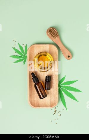 Estratto di olio di cannabis, semi di canapa e spazzola per massaggio viso su sfondo verde vista dall'alto. Olio cbd di marijuana medica. Trattamento di bellezza alternativo, alle erbe Foto Stock