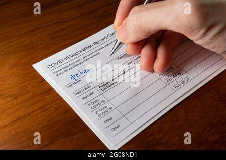 Scrittura di un nome su una scheda di registrazione della vaccinazione Covid-19 Foto Stock