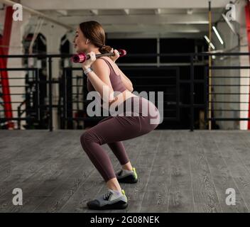 Una bella donna europea sbatte con un bar sulle spalle. Giovane ragazza in abbigliamento sportivo facendo esercizi sui muscoli delle natiche. Foto Stock