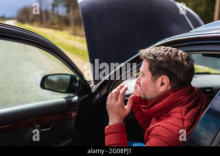 Uomo che chiama servizio di riparazione dopo auto breakdown.yoog uomo che parla su cellulare su strada. Auto rotta situazione. Foto Stock