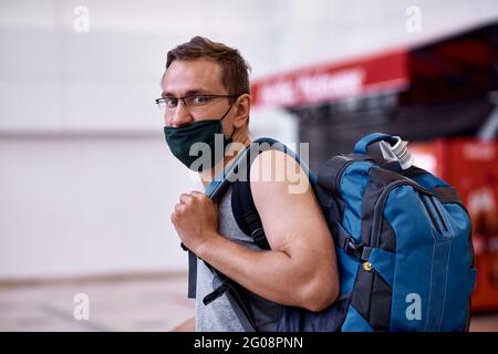 Passeggero mascherato con bagaglio nella lobby dell'aeroporto. Turismo durante una pandemia di coronavirus. Sfondo sfocato. Foto di alta qualità Foto Stock