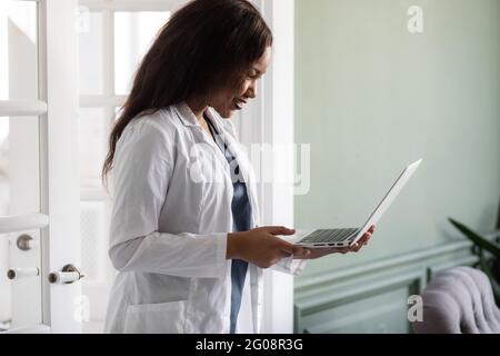 Bella contented afroamericana donna medico lavorando su un portatile. telemedicine Foto Stock
