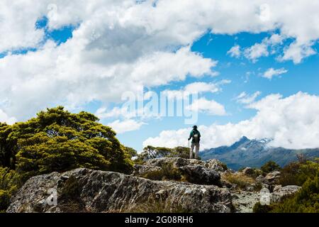 Un uomo in piedi sulla cima del Key Summit sotto le lunghe nuvole bianche, Routeburn Track, South Island. Foto Stock