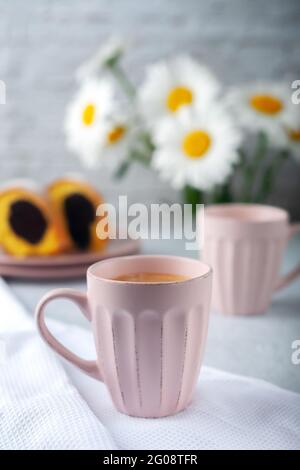 Due tazze di caffè appena fatto con crema con cupcake e fiori di camomilla Foto Stock