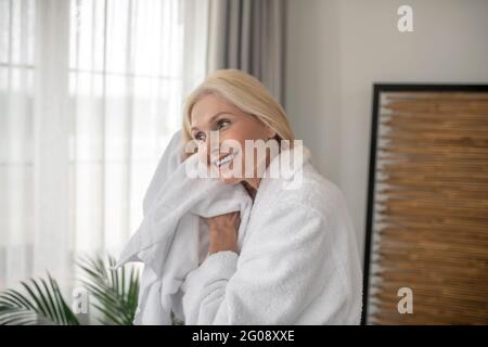 Donna bionda sorridente che asciuga i capelli con un asciugamano dopo il bagno Foto Stock
