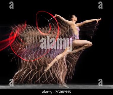 Giovane bella ragazza ginnastica ritmica in movimento isolata in luce mista su sfondo scuro. Stroboscopio Foto Stock