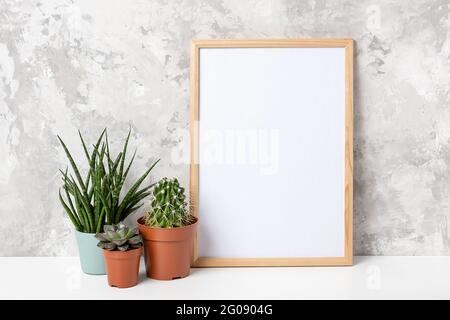 Telaio verticale in legno con cartoncino bianco e fiori verdi di piante da casa in pentola su tavolo su fondo grigio parete in cemento. Modello di mockup per il Foto Stock