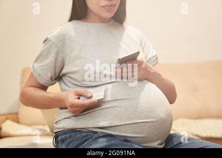 Donna incinta a casa con il telefono è seduto con il carrello di credito, concetto: Shopping online. Foto di alta qualità Foto Stock