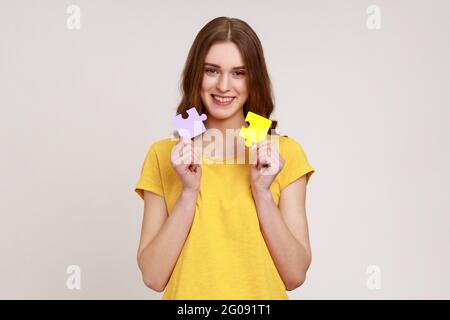 Sorridente ragazza in T-shirt casual tenendo e mostrando due pezzi di puzzle jigsaw, corrispondenza e collegare puzzle, risolvere i problemi con un buon risultato. Indù Foto Stock