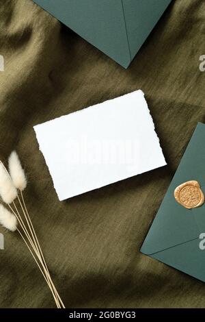 Cancelleria vintage per matrimoni con vista dall'alto. Biglietto d'invito bianco rustico, buste, fiori secchi su tessuto verde. Disposizione piatta, vista dall'alto, spazio per la copia. Foto Stock