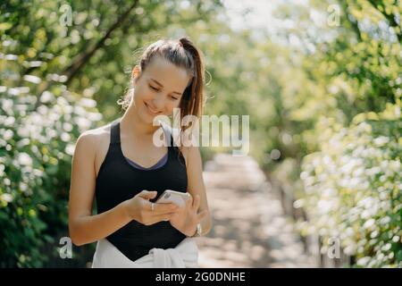 Felice atletica giovane donna utilizza smartphone sport tracker applicazione utilizza dispositivi moderni per la salute e fitness essere intelligente circa l'allenamento pose Foto Stock
