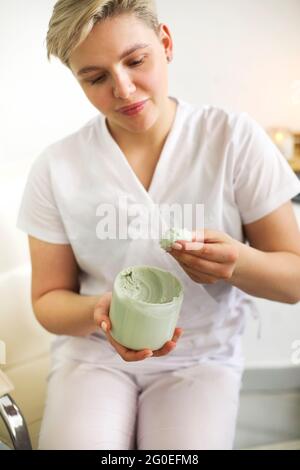 Alto angolo di raccolto anonimo cosmetologa femminile con vaso di crema verde nutriente nel salone di bellezza Foto Stock