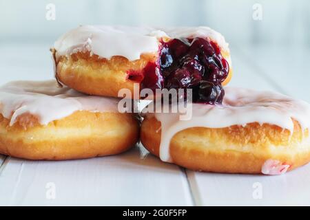 Ciambelle di vaniglia ghiacciate riempite di ripieno di mirtillo. Messa a fuoco selettiva con primo piano e sfondo sfocati. Foto Stock