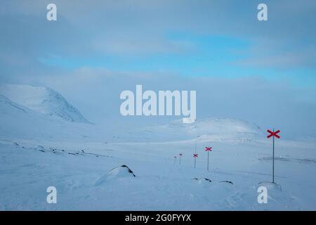 Lasciando le cabine Alesjaure la mattina presto mentre racchette da neve Kungsleden Trail, Lapponia, Svezia 2021 aprile. Le croci rosse segnano il sentiero. Foto Stock