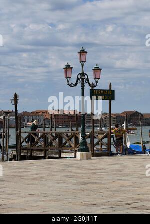 Strassenlaterne am Eingang zum Markusplatz in Venedig neben einer menschenleeren Anlegestelle gegen den bewölkten Himmel Foto Stock