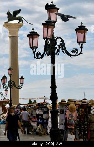 Vierarmige Strassenlaterne am Eingang zum Markusplatz in Venedig vor dem Wahrzeichen, dem Markuslöwen, und Verkaufsständen gegen den bewölkten Himmel Foto Stock