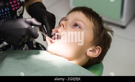 Viso del ragazzo in sedia dentale con le mani del dentista in guanti con attrezzo Foto Stock