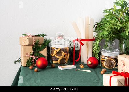 Tavolo festoso decorato Natale o Capodanno, rami thuja e abete rosso, candele e palle di Natale, biscotti al cioccolato in un vaso e scatole regalo Foto Stock