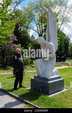 L'uomo anziano si trova accanto all'angelo di marmo all'ingresso del cimitero di St. Hedwig, Alter Domfriedhof St. Hedwig, Berlino. Foto Stock