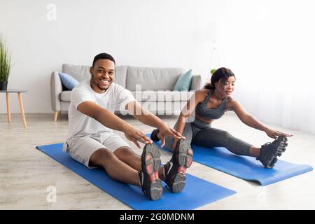 Giovane coppia afroamericana che si allunga sui tappetini yoga, facendo allenamento domestico, facendo esercizi di flessibilità a casa Foto Stock