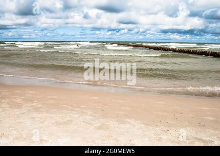 Paesaggio di spiaggia e mare con onde, cielo nuvoloso, frangiflutti. Costa del Mar Baltico vicino a Leba in Polonia. Foto Stock