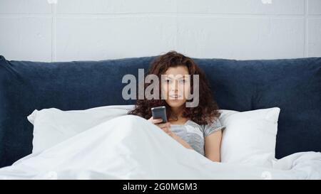 felice giovane donna che tiene il telecomando a letto Foto Stock