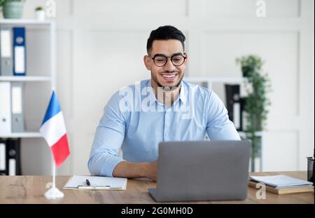 Tutoring online in lingue straniere. Allegro insegnante arabo maschile che dà classe francese, comunicando su laptop da casa Foto Stock