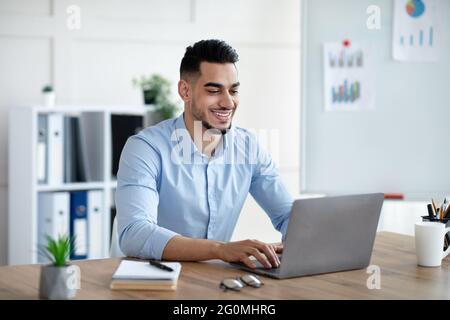 Bel giovane uomo d'affari arabo che lavora con un computer portatile alla sua scrivania in ufficio Foto Stock