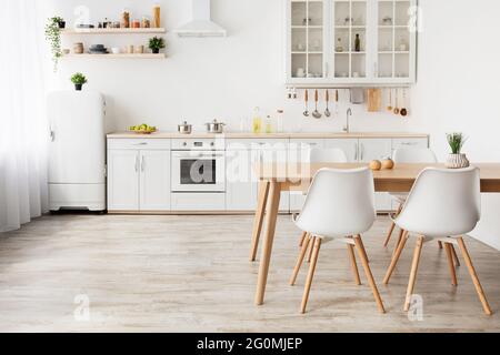 Cucina leggera in stile scandinavo. Tavolo da pranzo in legno e mobili bianchi, piccolo frigorifero, spazio vuoto Foto Stock