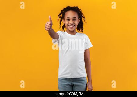 Felice ragazza nera gesturing pollici su e sorridente Foto Stock