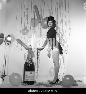 Champagne negli anni '50. Una giovane donna in una scena che chiaramente è destinata a suggerire qualcosa da celebrare. Una bottiglia gigante di champagne Delck fa parte dell'arredamento, palloncini e confetti appesi sullo sfondo. Svezia 1952 rif BK84-4 Foto Stock