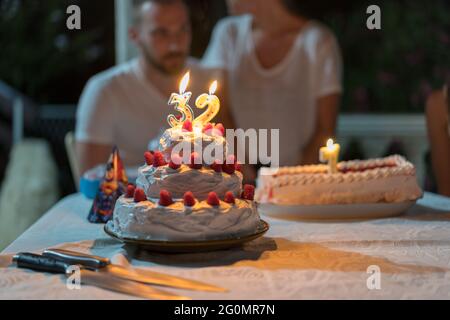 Ragazzo che festeggia il suo trentaduesimo compleanno. Torta con fragole e frutta. Coltelli e cappelli da festa sul tavolo Foto Stock