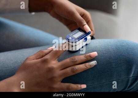 Donna nera irriconoscibile che utilizza la clip del pulsossimetro sul dito a casa Foto Stock