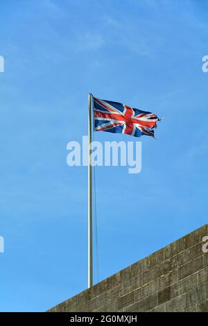 Bandiera di Union Jack che vola in alto in una giornata ventosa contro un cielo blu chiaro. Foto Stock