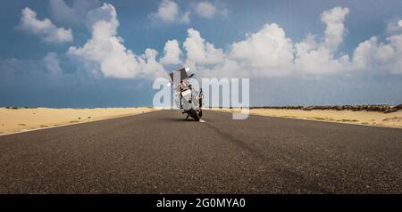 Moto in piedi su strada nera catrame con cielo blu che dà l'esperienza di guidare da solo sulla linea di costo. Foto Stock