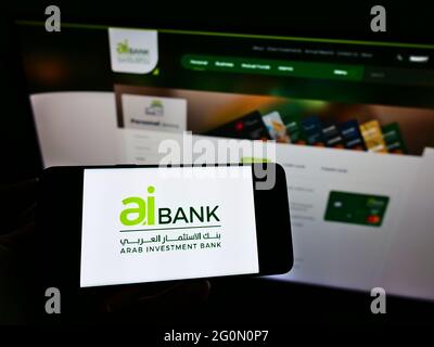 Persona che detiene cellulare con logo della società finanziaria Arab Investment Bank (AIB Egitto) sullo schermo di fronte alla pagina web. Mettere a fuoco il display del telefono. Foto Stock