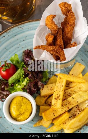 Pollo fritto e patatine fritte su piatto blu con birra Foto Stock