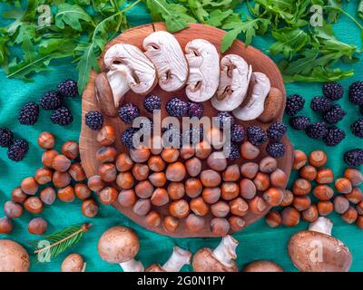 Una sana selezione di cibo autunnale: Funghi bianchi a fette, nocciole sgusciate, insalata di rucola, more e piccolo ramo di abete su sfondo verde. Foto Stock