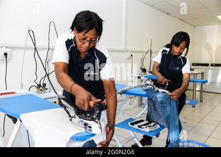 JOHANNESBURG, SUDAFRICA - 03 febbraio 2021: Johannesburg, Sudafrica - 2 ottobre 2012: Giovane donna nera che stira l'abbigliamento del cliente in una lavanderia automatica Foto Stock
