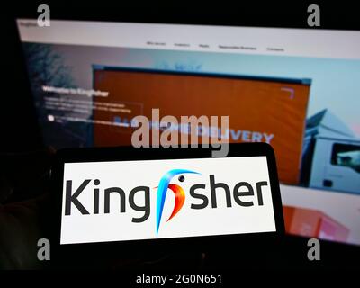 Persona che tiene il cellulare con il logo commerciale della società britannica al dettaglio Kingfisher plc sullo schermo di fronte al sito web. Mettere a fuoco il display del telefono. Foto Stock